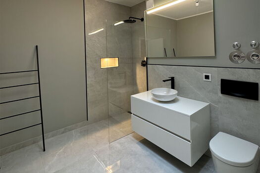 Modernes, minimalistisches Badezimmer mit einem schwebenden weißen Waschtisch, einem Gefäßwaschbecken, einer wandmontierten Toilette, einer offenen Glasdusche, schwarzen Armaturen, einem Handtuchhalter und einem großen Spiegel auf hellgrauen Wänden und Bö